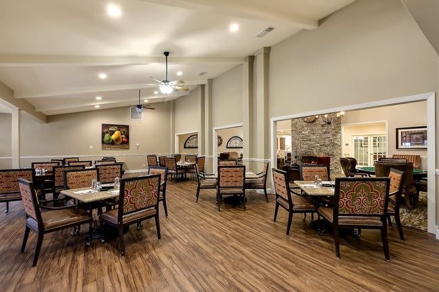 A spacious dining room with elegant tables and chairs, featuring warm lighting and hardwood flooring.
