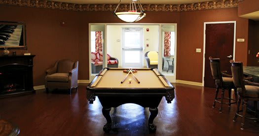 A recreation room featuring a pool table under a chandelier, with seating areas and bright decor.