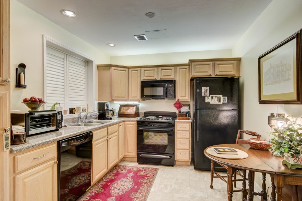 A cozy kitchen with light wood cabinets, black appliances, and a small dining area.