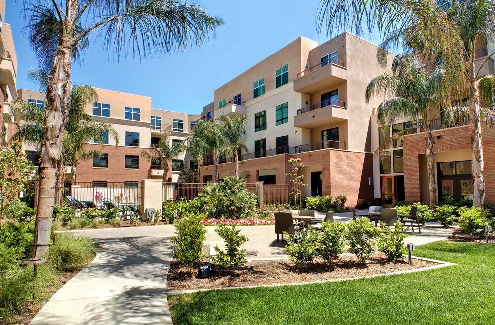 A modern apartment building surrounded by lush landscaping and palm trees on a sunny day.