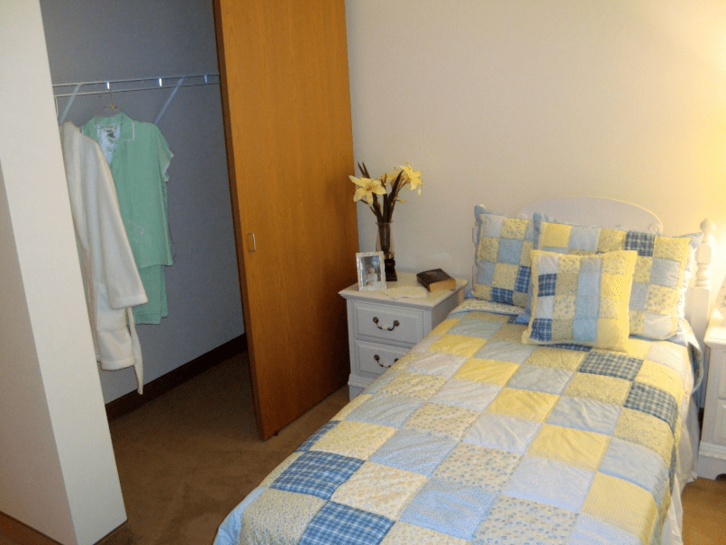 A cozy bedroom with a quilted bedspread, nightstand, and partially open closet.