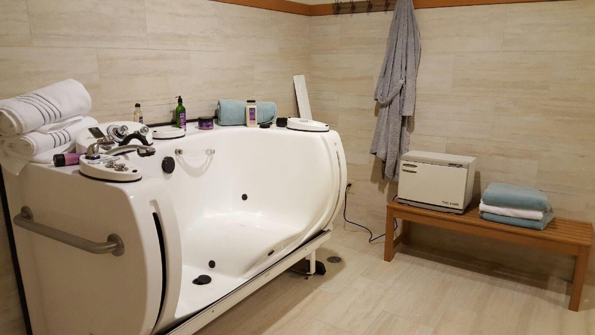 A modern bathroom featuring a white bathtub, a wall-mounted robe, and various toiletries on a nearby bench.