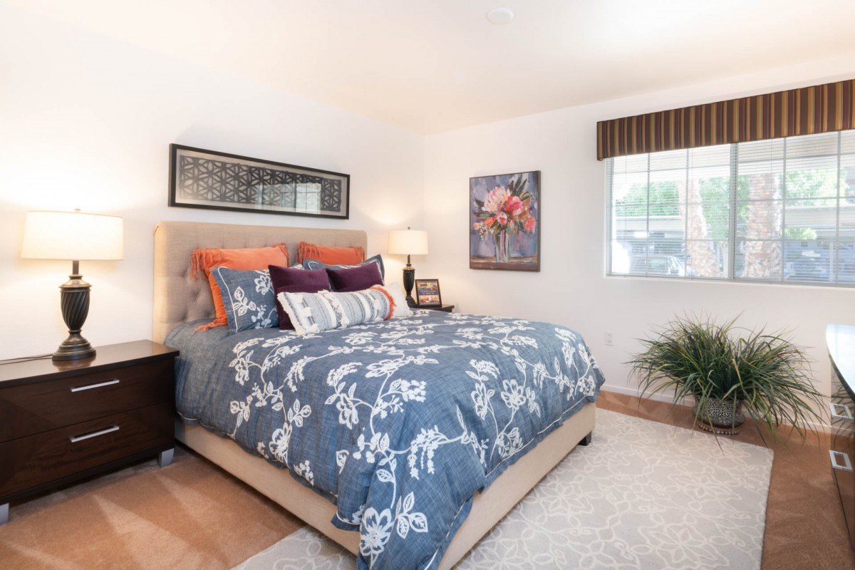 A cozy bedroom with floral bedding and vibrant pillows, featuring artwork and a window for natural light.