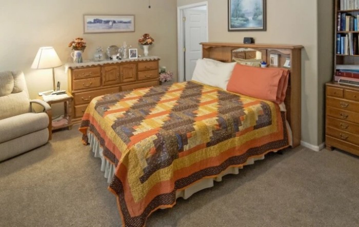 A cozy bedroom with a colorful quilt on the bed and wooden furniture.