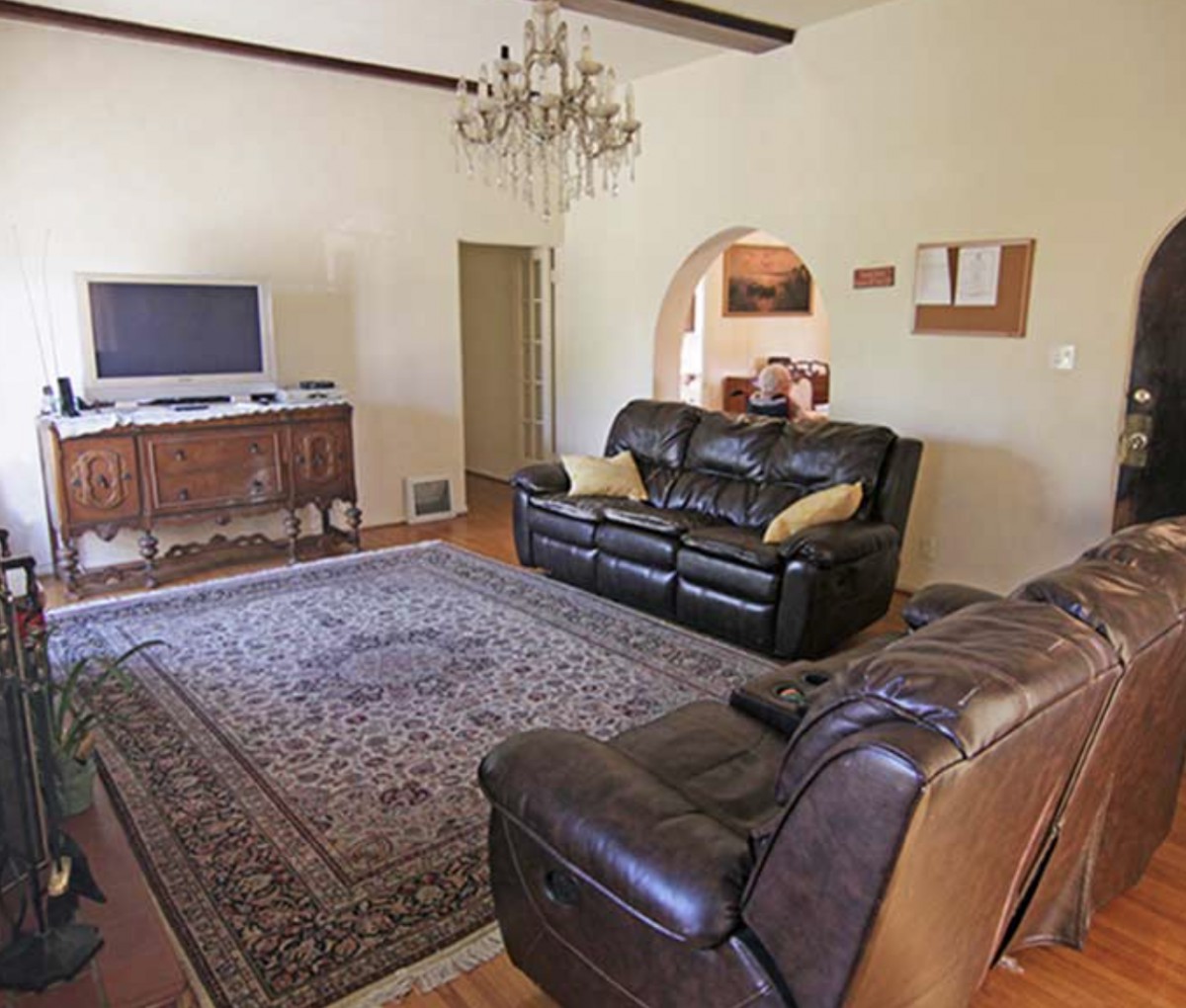 A cozy and spacious living room with leather sofas, a large rug, and a chandelier.