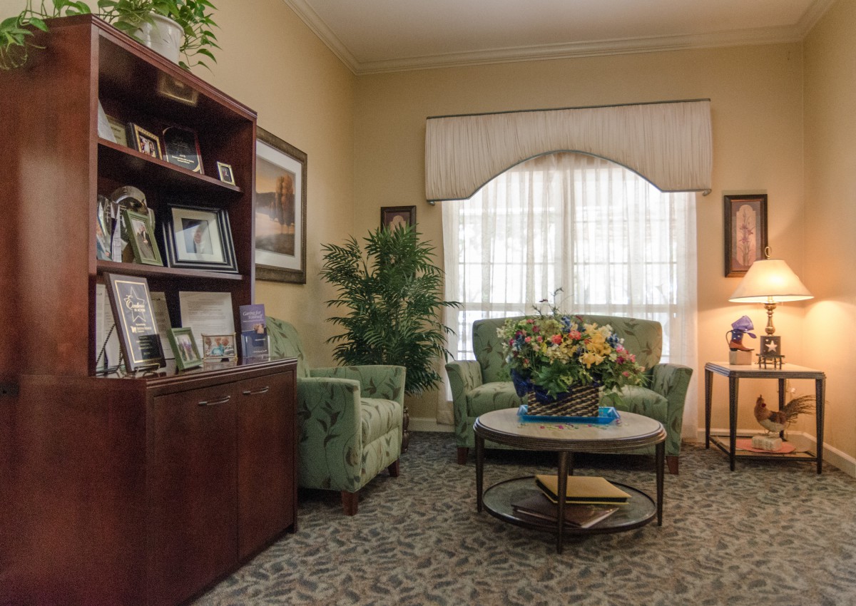 A cozy living room featuring green armchairs, a wooden coffee table adorned with flowers, and a bookshelf filled with framed photos.