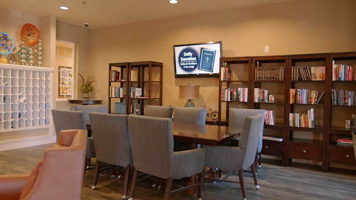 A cozy meeting room with a table surrounded by chairs, bookshelves filled with books, and a television mounted on the wall.