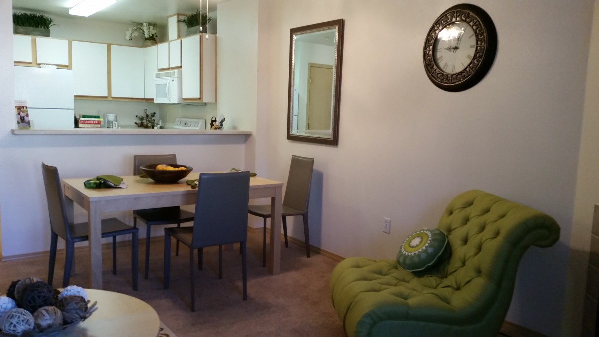 A cozy living and dining area with a green sofa and a wall clock.