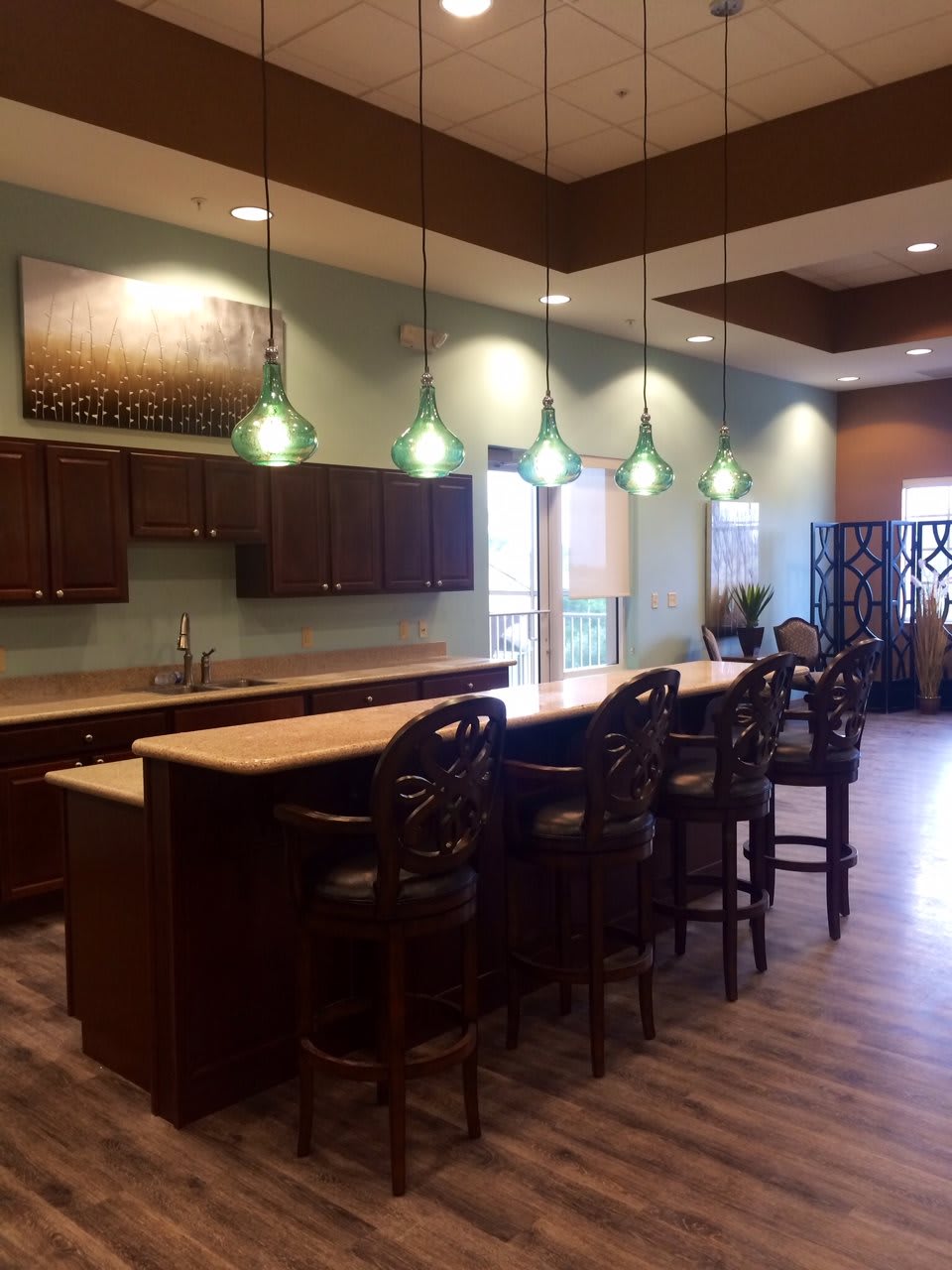 A modern kitchen interior with a large countertop and bar stools, illuminated by pendant lights.