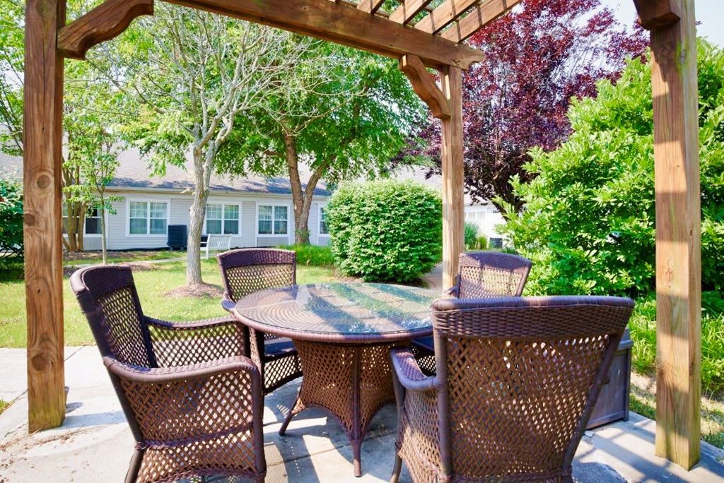 A cozy outdoor patio with wicker furniture under a wooden pergola, surrounded by lush greenery.