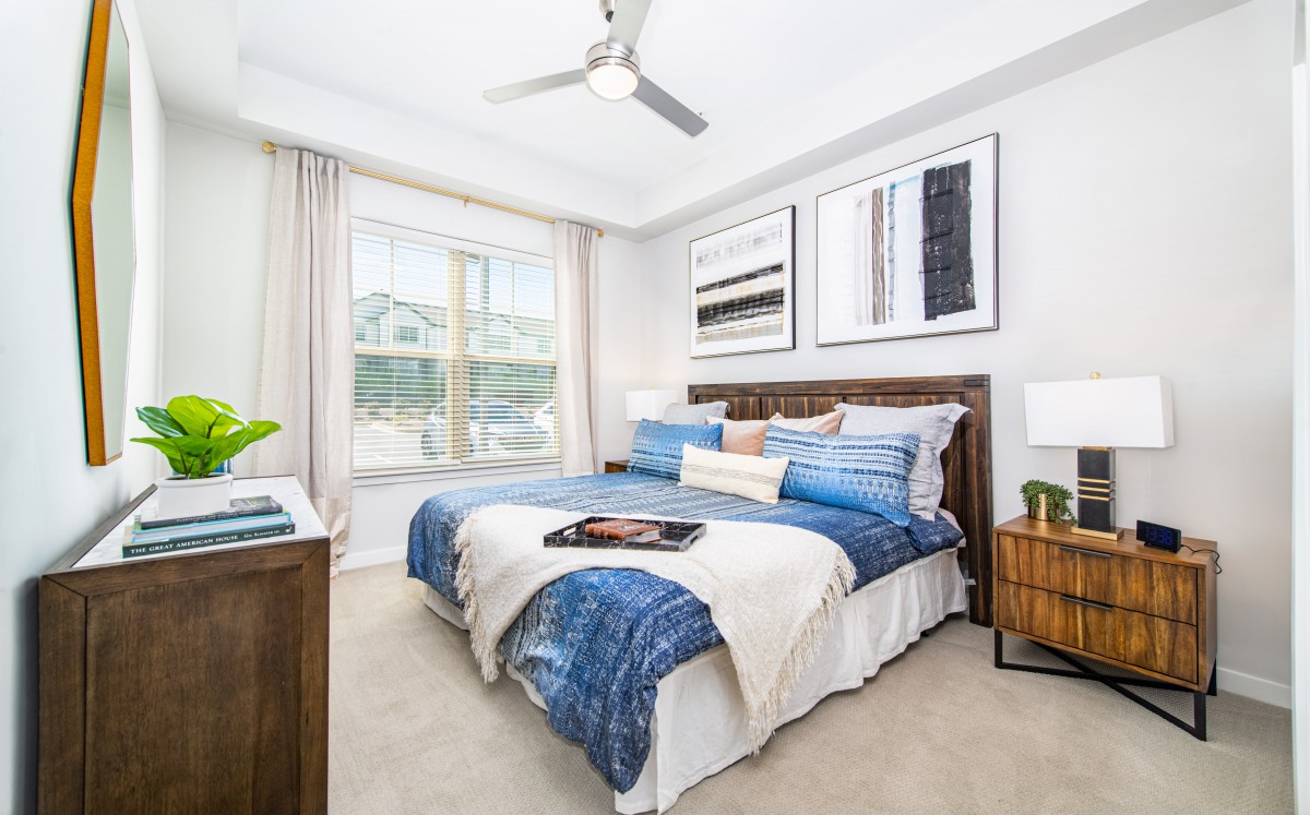 A modern bedroom with stylish decor, featuring a bed with blue bedding, wall art, and a ceiling fan.