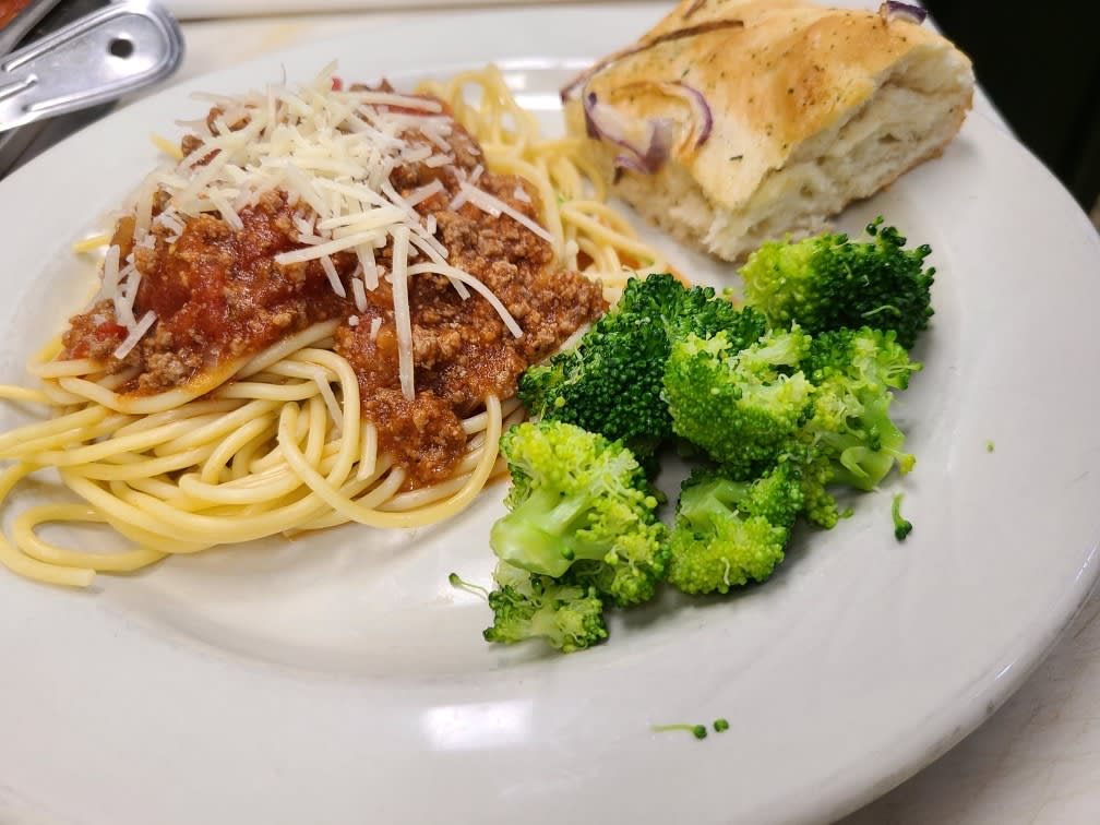 A plate of spaghetti bolognese served with bread and broccoli.