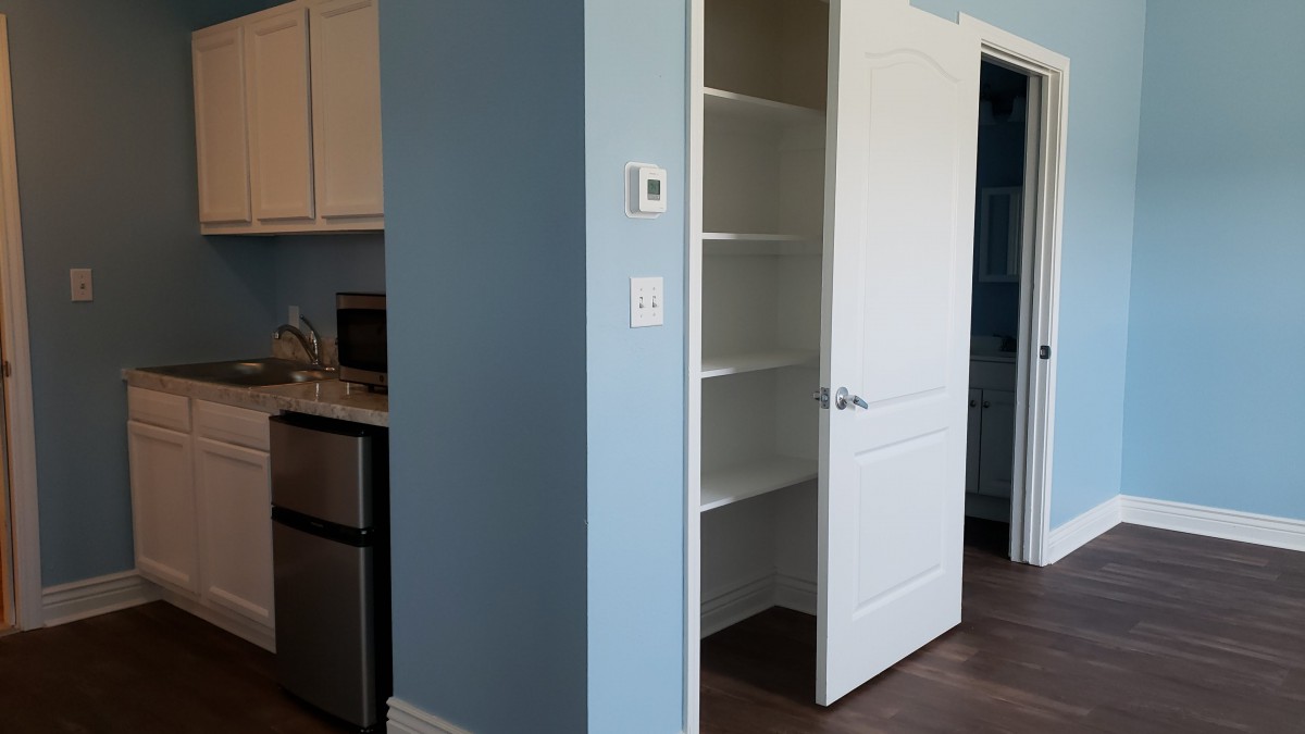 An empty pantry with open shelves next to a kitchen area, featuring a blue wall.