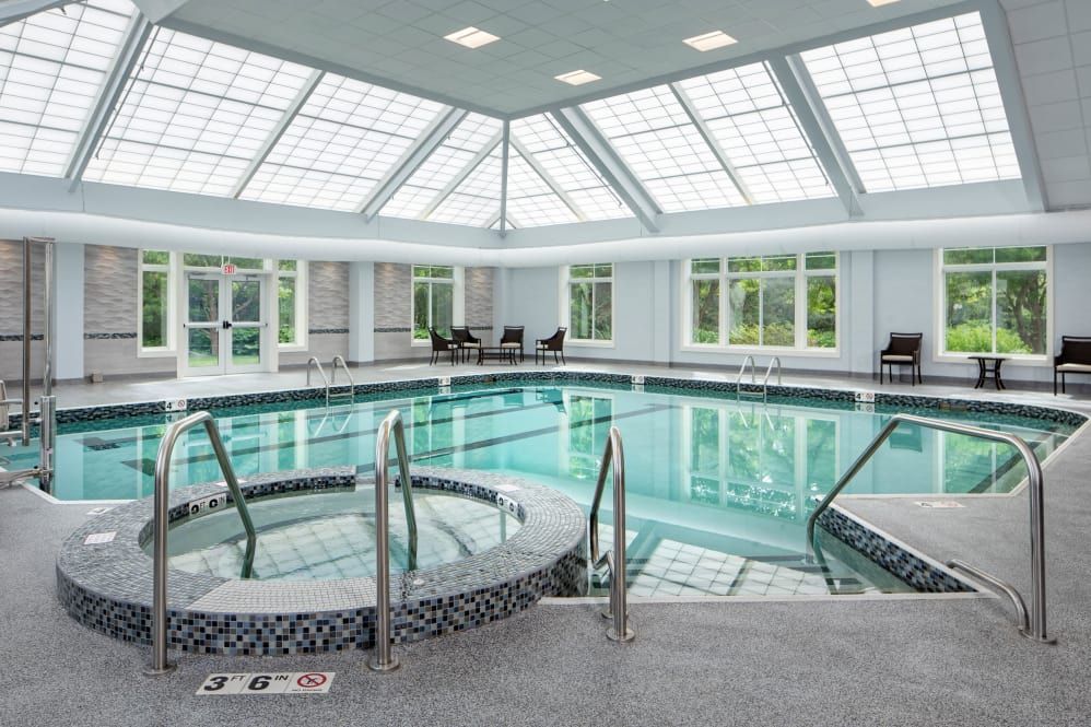 A modern indoor swimming pool with a connected hot tub under a skylight ceiling.