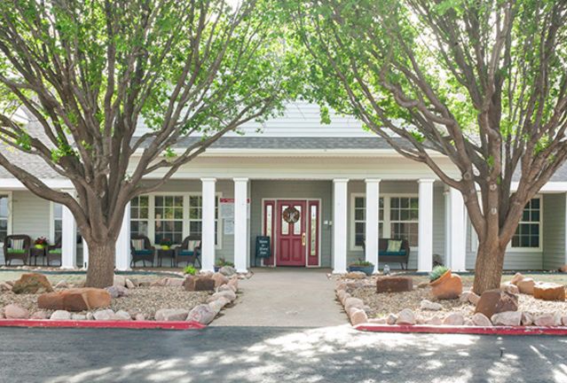 A charming house entrance with a porch and columns, surrounded by trees and landscaping.