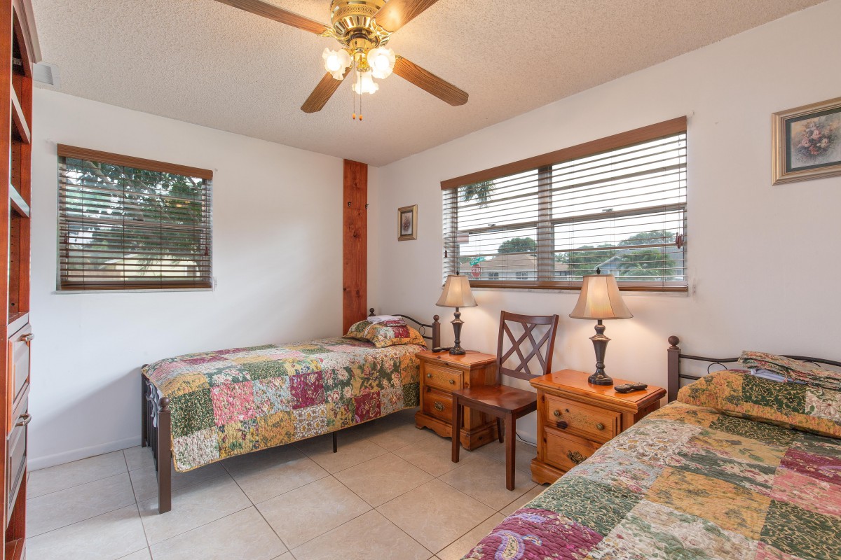 A cozy bedroom featuring two twin beds with colorful quilts, wooden furnishings, and ample natural light.