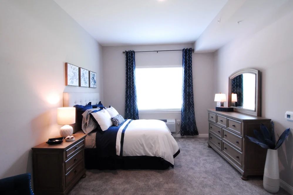 A cozy bedroom with a neatly made bed, dresser, and soft lighting.