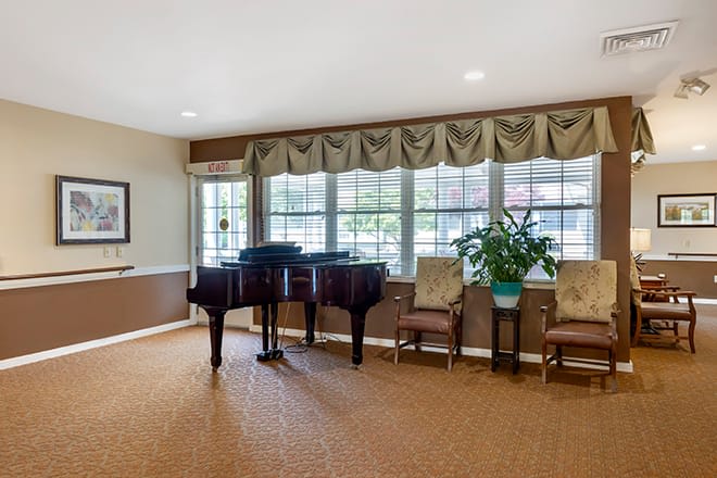 A cozy room with a grand piano, chairs, and large windows adorned with curtains.