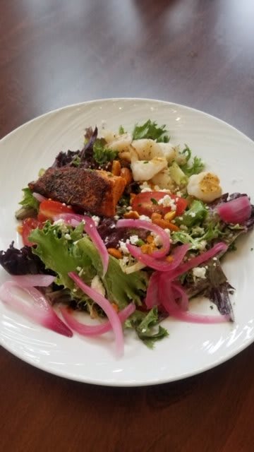 A healthy salad with mixed greens, grilled salmon, cauliflower, red onions, and vegetables.