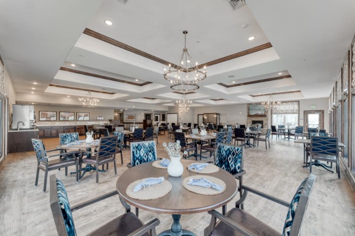 A spacious and elegantly designed dining area with a chandelier, neatly arranged tables and chairs.
