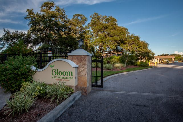 Entrance gate with a sign for Bloom surrounded by lush greenery.