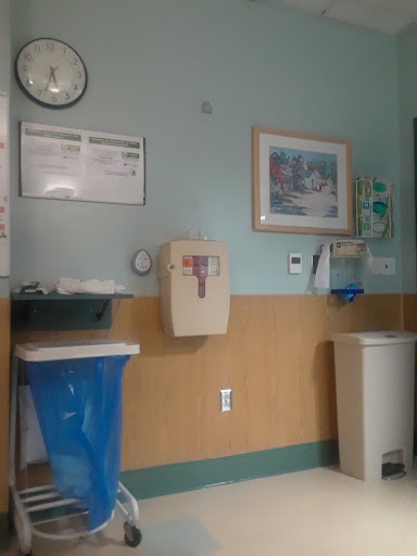 A view of a hospital room featuring a clock, wall art, and various medical waste disposal units.