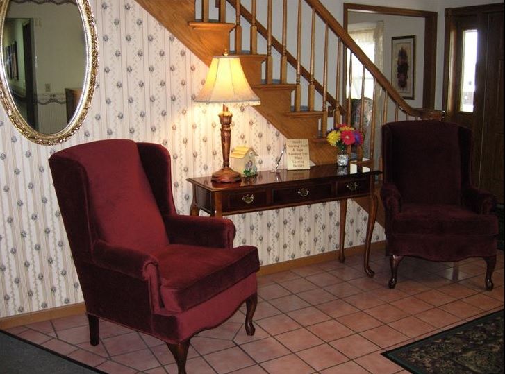A cozy living room corner featuring two red armchairs, an elegant table with a lamp, and a staircase in the background.