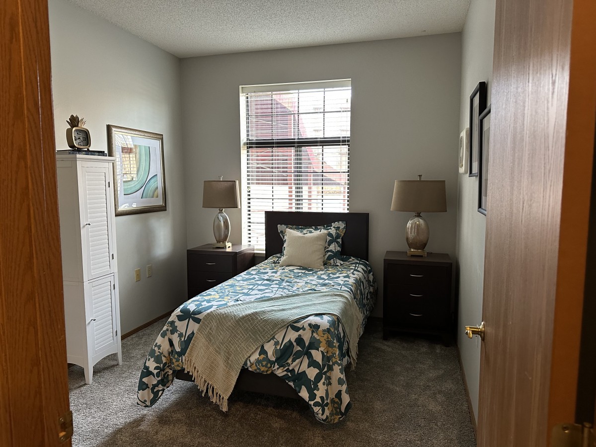 A cozy bedroom with a single bed, twin lamps, and a window letting in natural light.