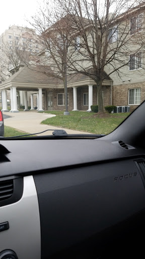 A view from the interior of a car, showcasing a building with a driveway and surrounding greenery.