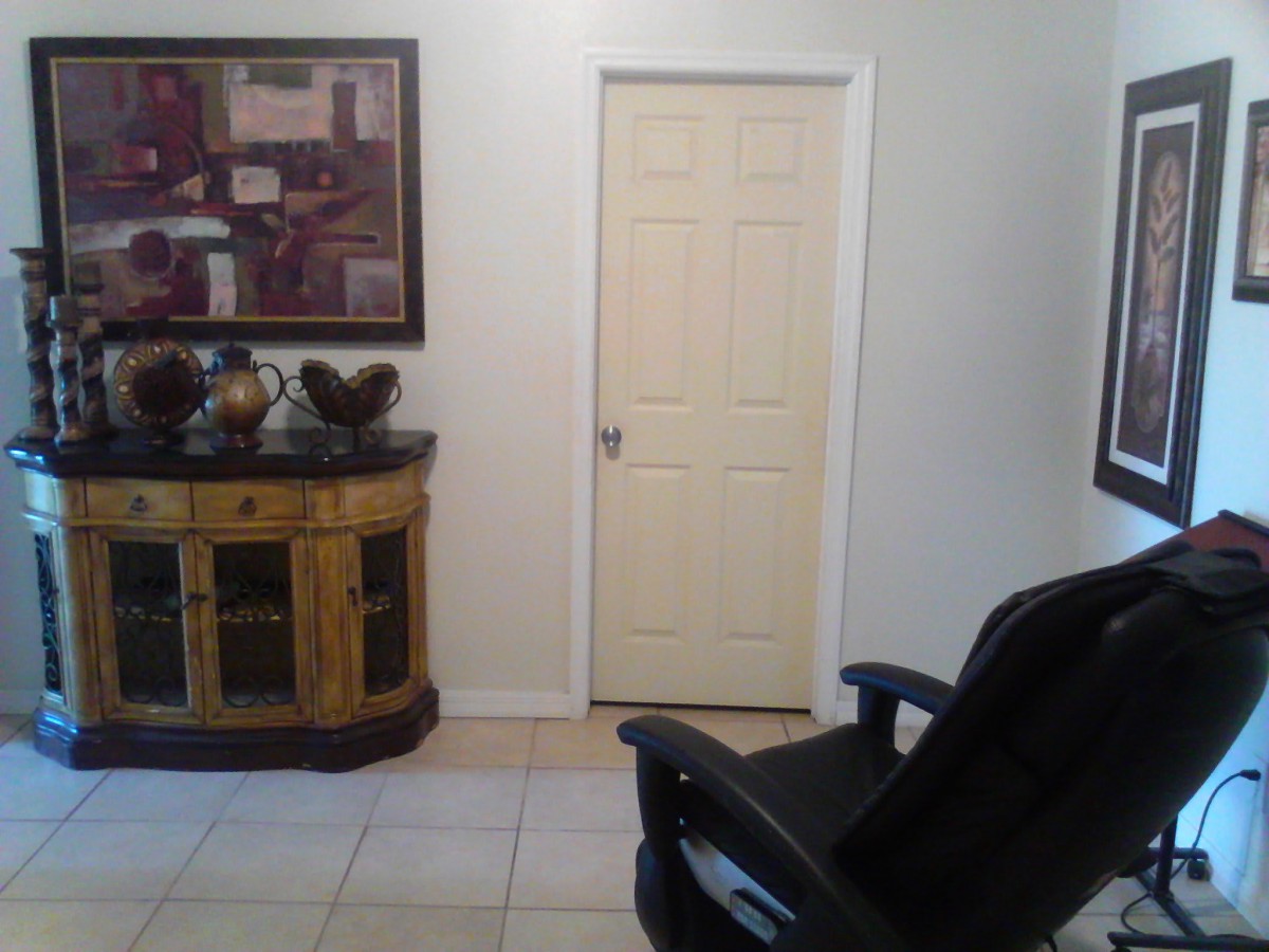 A room with a closed door, an office chair, a decorative cabinet, and artwork on the wall.