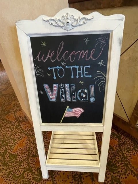 A decorative chalkboard sign welcoming guests with a patriotic theme, featuring an American flag.