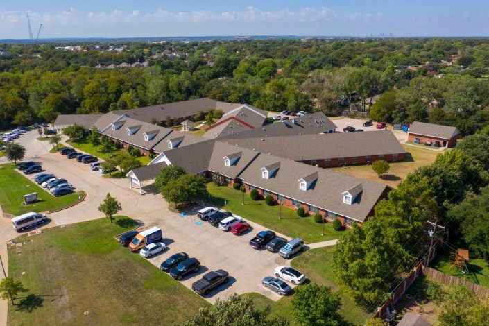 Aerial view of a building complex with a parking lot and surrounding trees.