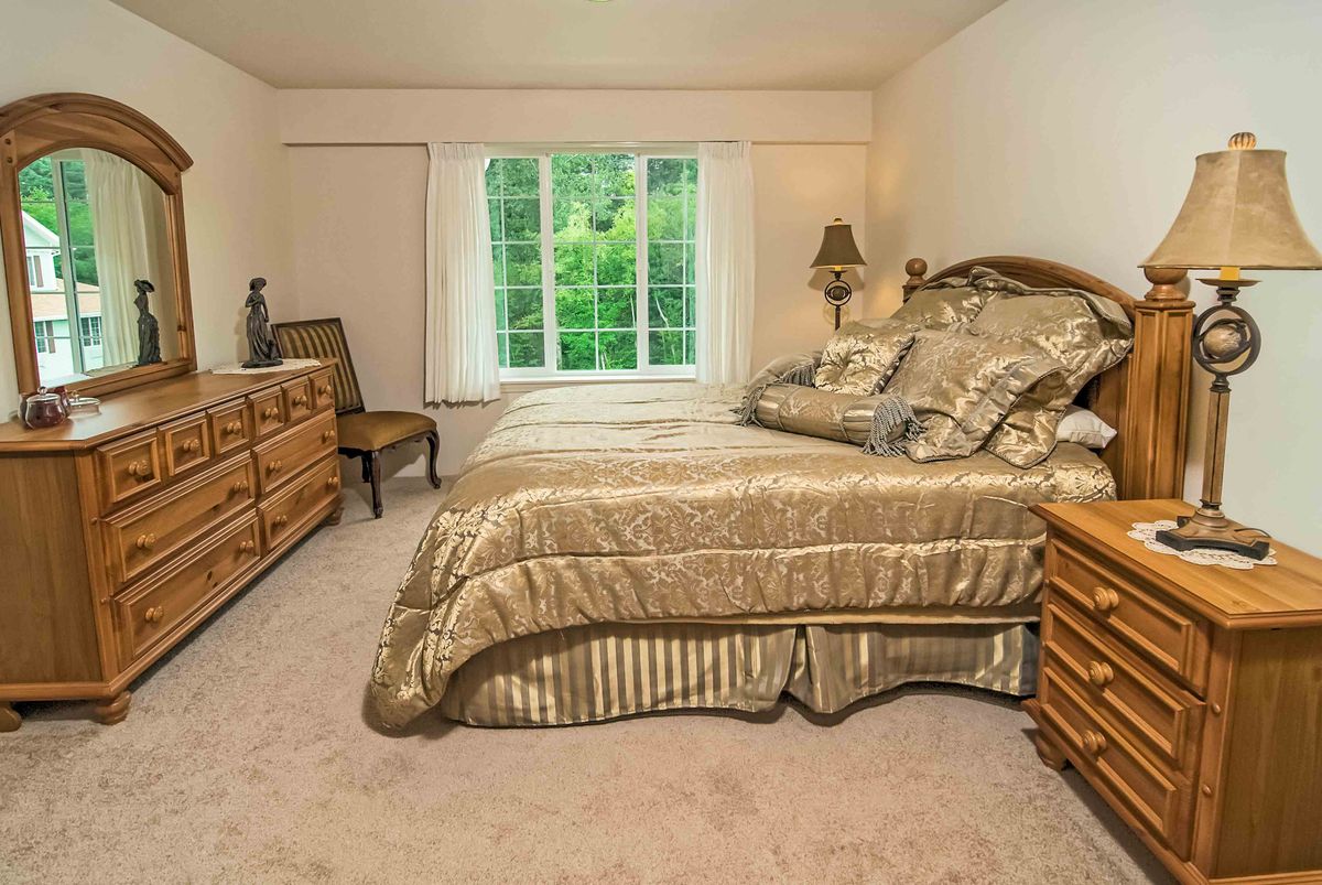 A neatly arranged bedroom with a large bed, wooden furniture, and a window with drapes.