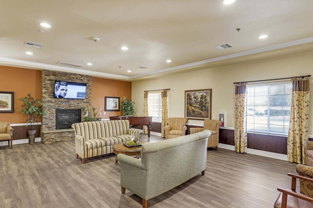 A cozy and well-furnished living room with comfortable seating, a TV above the fireplace, and large windows providing ample natural light.