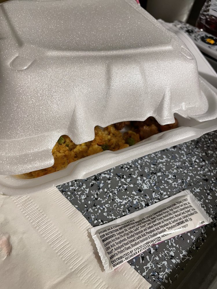 A partially opened foam takeout container with food inside, resting on a table next to a napkin.