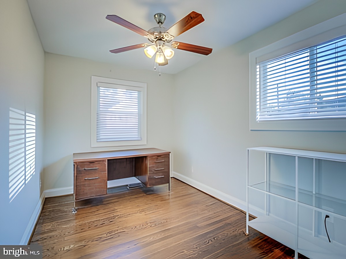 A minimalist empty room with a wooden desk, ceiling fan, and wooden flooring.