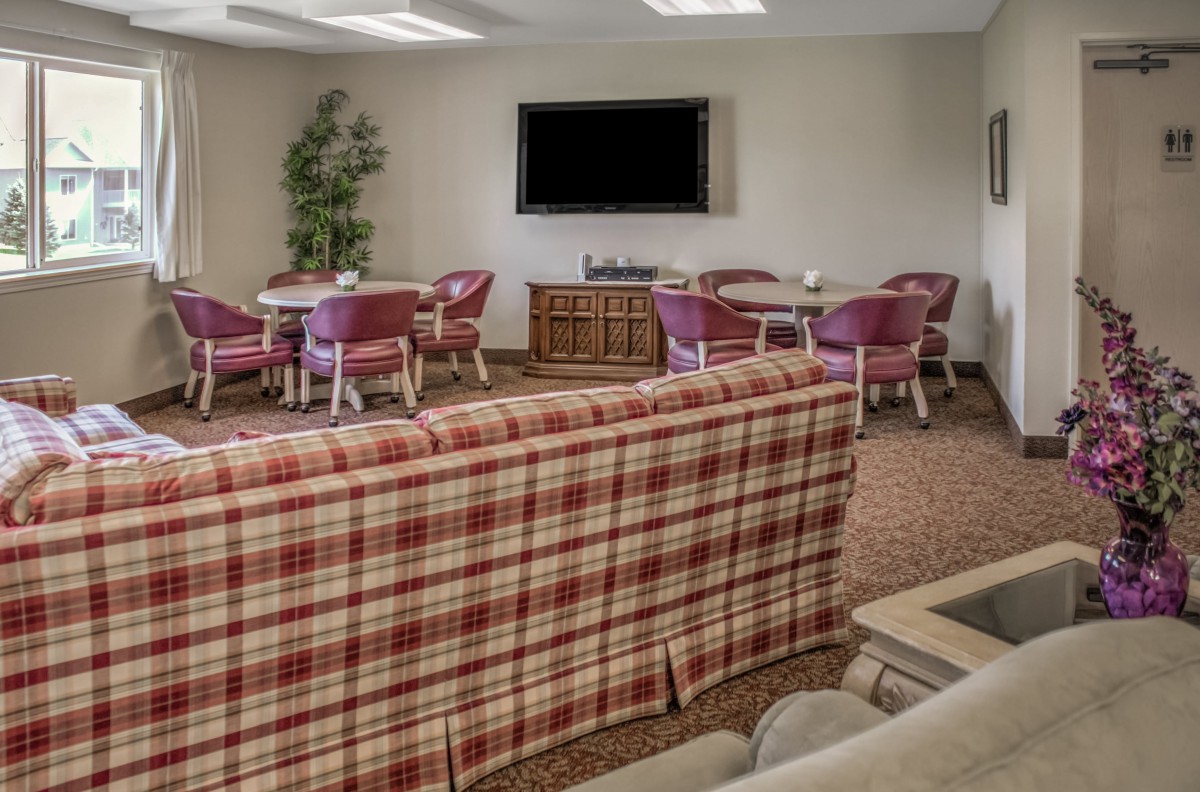 A cozy living room with a plaid sofa, multiple chairs, and a television on the wall.