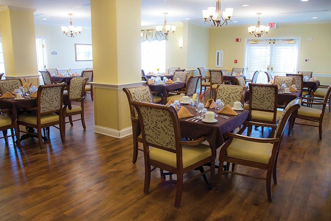 An elegant dining room with neatly arranged tables and chairs, featuring chandeliers and a wooden floor.