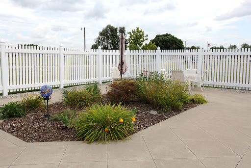 A peaceful garden area featuring various plants and flowers, enclosed by a white fence.
