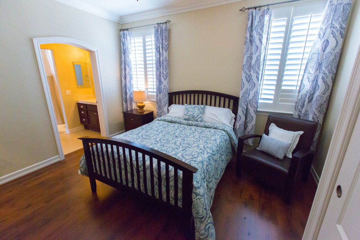 A cozy bedroom featuring a wooden bed with patterned bedding, an armchair, and elegant curtains.