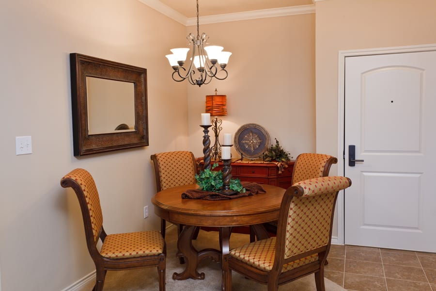 A cozy dining room with a round wooden table, upholstered chairs, and a decorative chandelier.