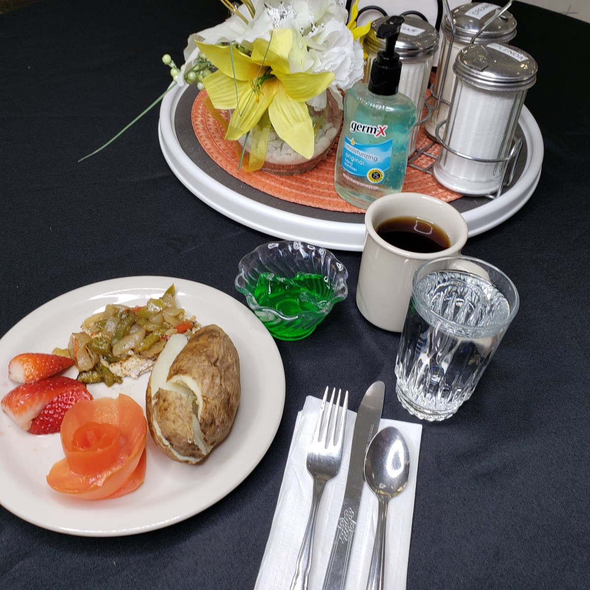 A meal served on a tray includes a baked potato, vegetables, coffee, and a jelly dessert.
