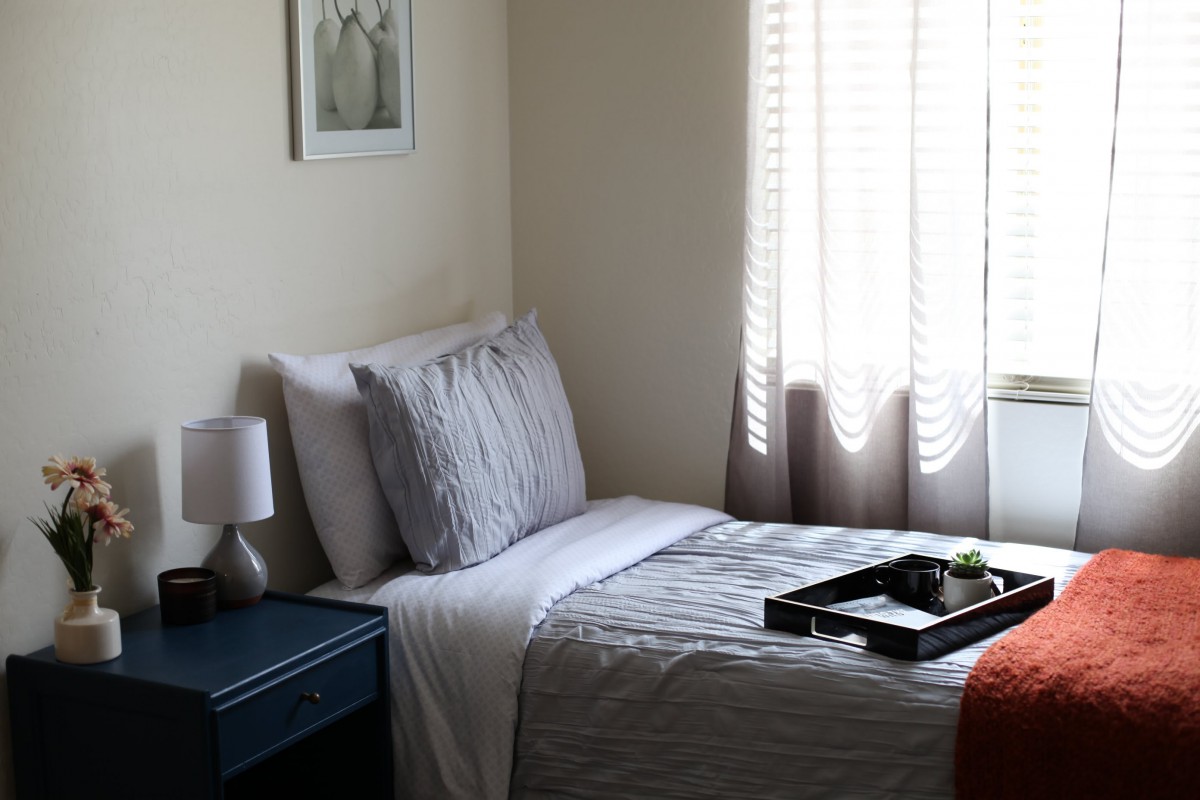 A cozy bedroom with a neatly made bed, bedside lamp, and window with blinds.