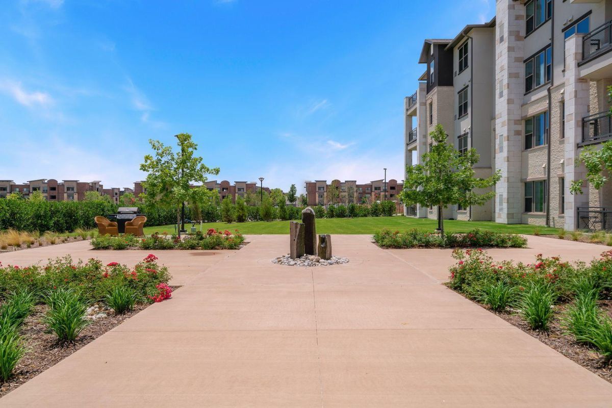 A modern building surrounded by a well-maintained garden and pathway under a clear blue sky.