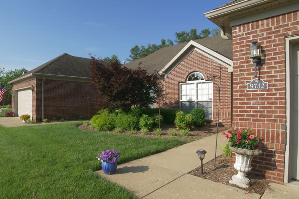 A well-maintained brick house with a landscaped garden and sidewalk under a clear blue sky.