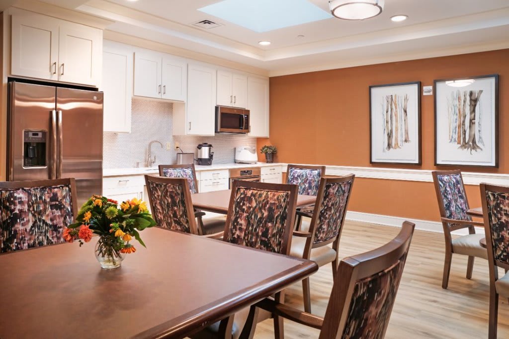 A modern kitchen and dining area featuring a wooden table with chairs, cabinetry, a microwave, and a decorative flower arrangement on the table.