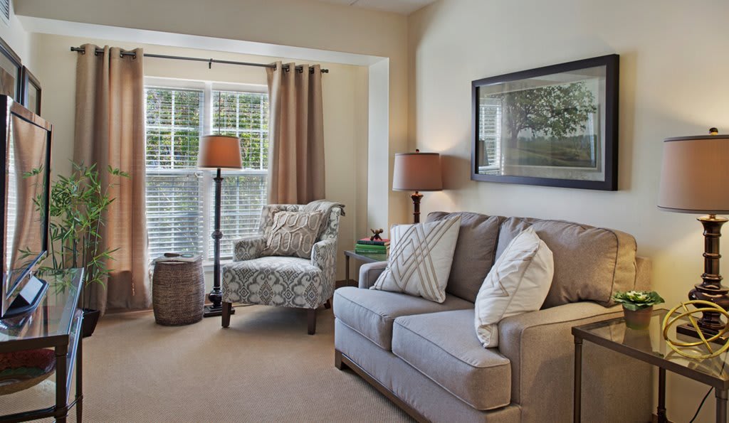 A cozy living room with a sofa, armchair, lamps, and a large window with curtains.