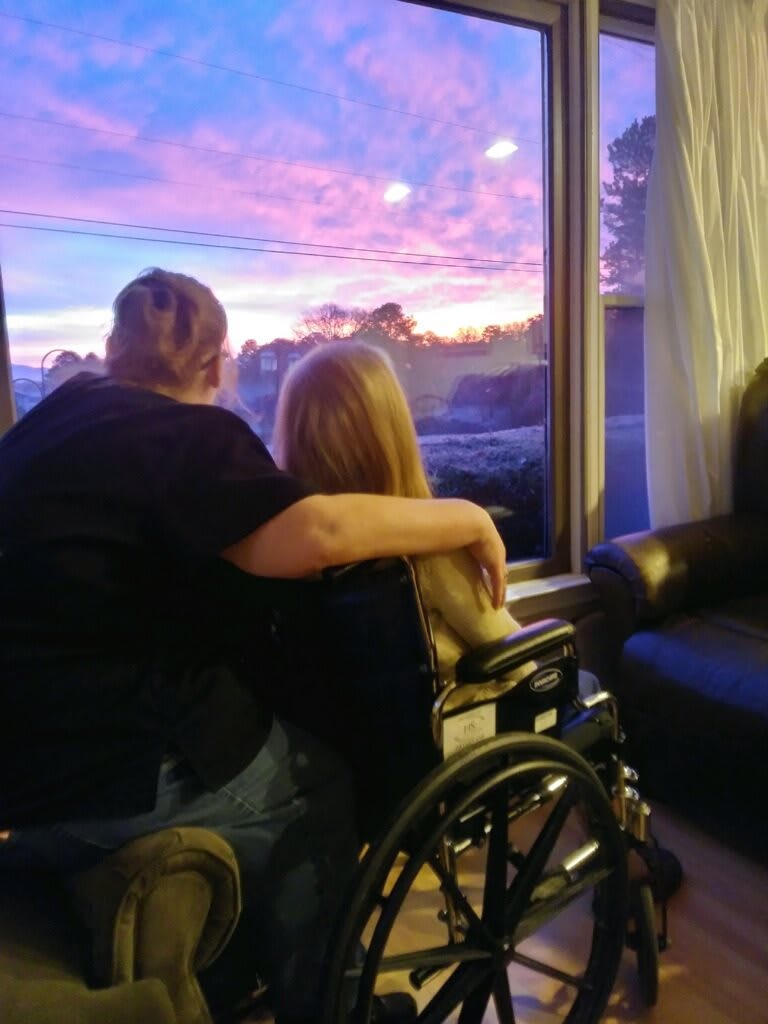 Two people share a tender moment, watching the sunset through a window.