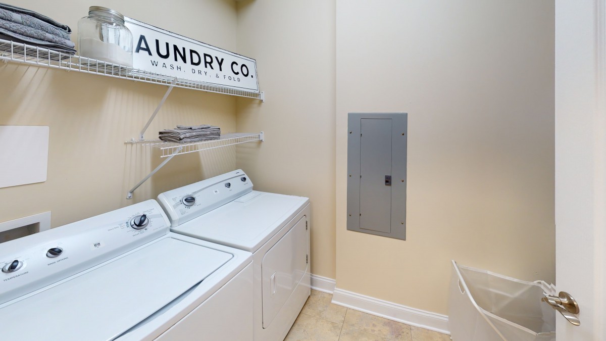A tidy laundry room with a washer and dryer, featuring a decorative wall sign.