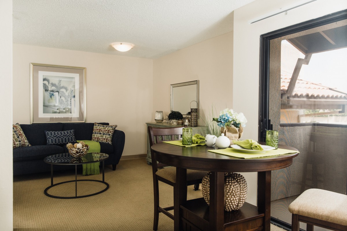 A cozy and elegantly designed living room featuring a round table with decorative items, a comfortable sofa with pillows, a large window, and tasteful artwork.